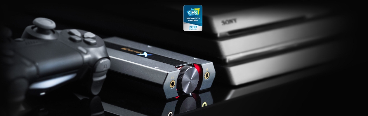 Placa de Som Externa USB Creative Sound BlasterX G6 em ângulo 3/4 ao lado de console PlayStation com selo CES Innovation Awards 2019