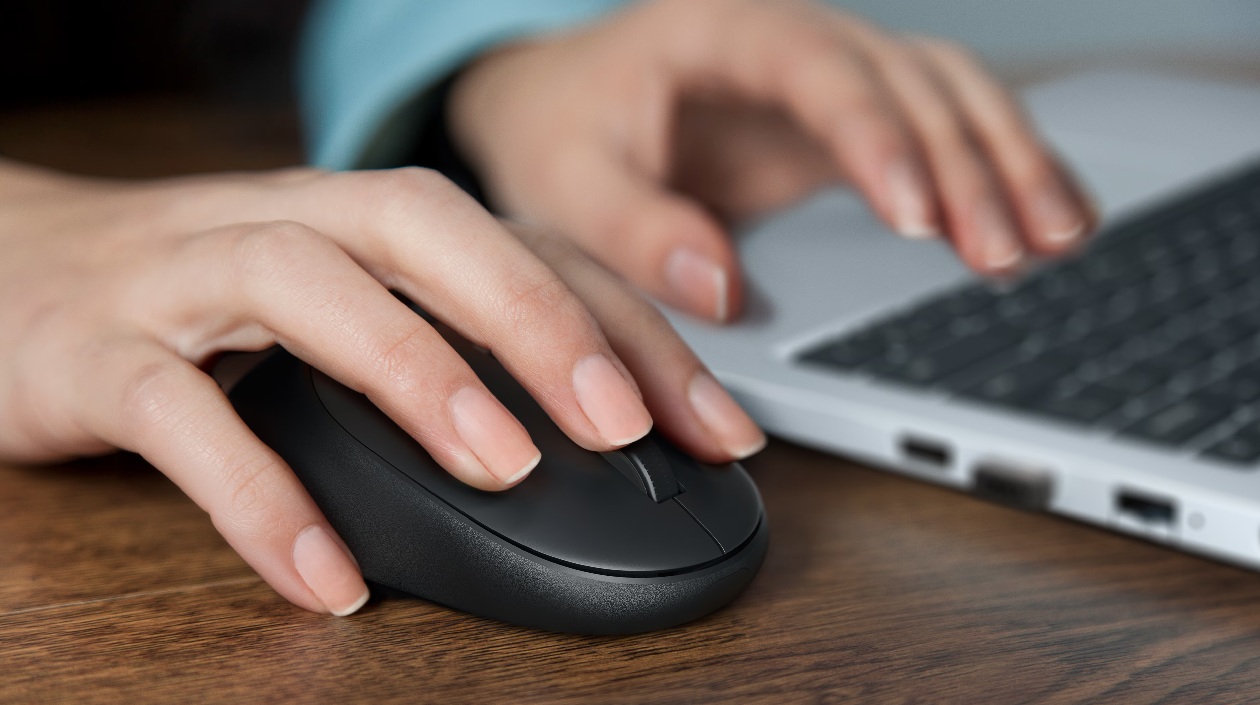 Mão do usuário sobre o mouse Dell Pro KM526 em estação de trabalho com notebook