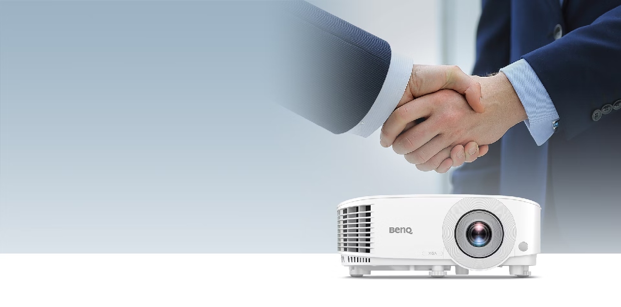 Aperto de mãos com projetor BenQ MX560C em primeiro plano simbolizando parcerias de sucesso e ferramenta indispensável para reuniões de alto impacto