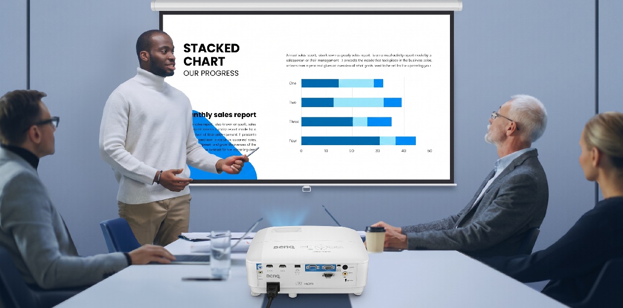 Palestrante utilizando apontador para apresentar gráficos de progresso em tela retrátil com projetor BenQ MX560C para equipe em sala de reuniões corporativa
