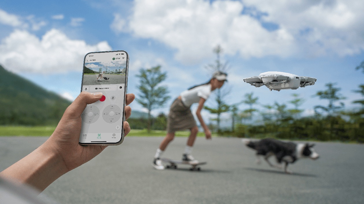 Controle manual via aplicativo de smartphone em primeiro plano com jovem de skate e cão ao fundo sendo filmados