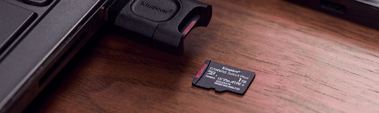 Cartão microSD Kingston 1TB ao lado de adaptador leitor USB conectado a um notebook